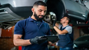Supervisor at a car workshop checking tablet while mechanic work.jpg