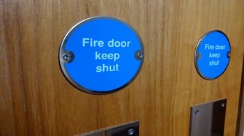 Photo showing a circular blue sign with white writing saying 'Fire Door Keep Shut'.jpg