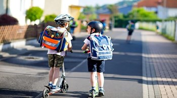 Two school kid boys in safety helmet riding with scooter in the city with backpack on sunny day.jpg