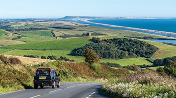 car-on-road-to-chesil-beach-dorset-with-patchwork-of-rolling-fields-and-sea-sml.jpg
